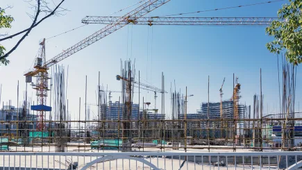Large active construction site in Qatar with tower cranes, scaffolding, and steel reinforcement structures under a clear blue sky, representing the type of high-value development sites where TrustForce Security provides professional construction site security guards across Qatar.