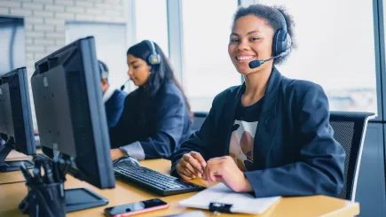 Friendly customer service operator wearing a headset at a computer workstation, representing the professional emergency call and service centre support available through TrustForce Security's technical security solutions in Qatar.