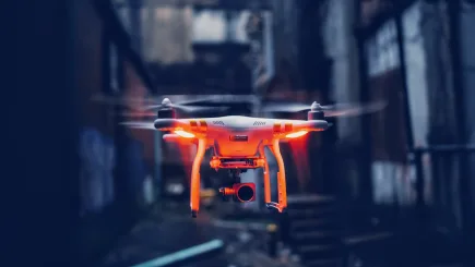 A camera-equipped surveillance drone in flight against a dark urban backdrop, representing the advanced surveillance technologies deployed by TrustForce Security as part of its technical security solutions in Qatar.